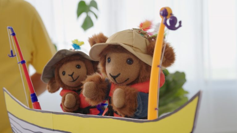 Biscuit et Cassonade, les deux personnages en peluche, pêchent dans un bateau de carton