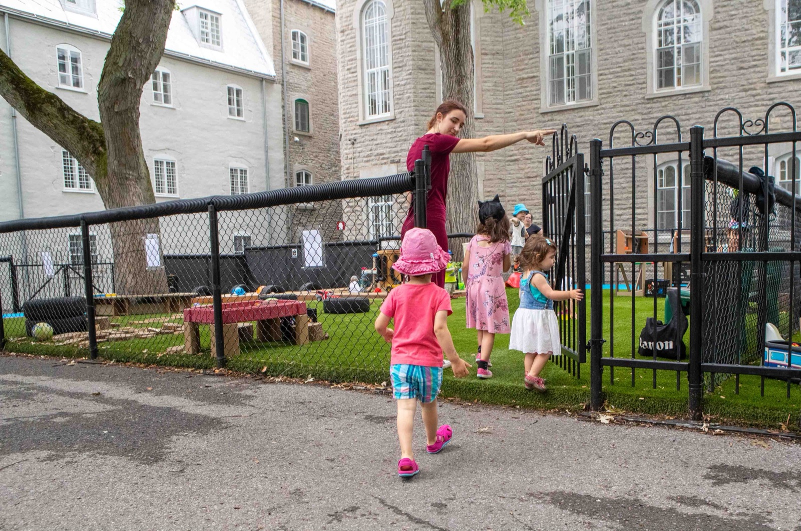Une éducatrice ouvre la barrière de la cour et accueille des enfants qui arrivent au service de garde